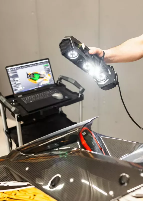 Operator skanuje karbonowy element pojazdu skanerem 3D Go!SCAN SPARK, a&nbsp;model pojawia się na laptopie