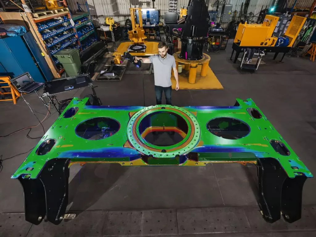 Operator skanuje dużą ramę stalową skanerem HandySCAN 3D MAX; kolorowa mapa odchylek na powierzchni