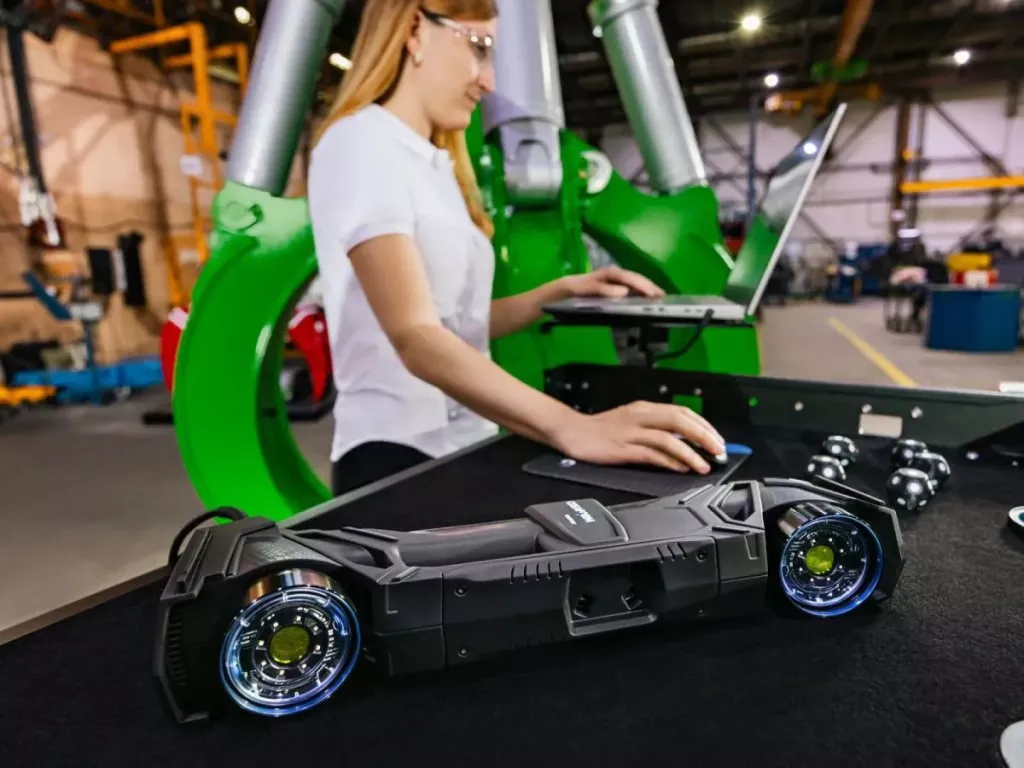 Zbliżenie skanera HandySCAN 3D MAX na stole; w&nbsp;tle operatorka pracuje przy laptopie