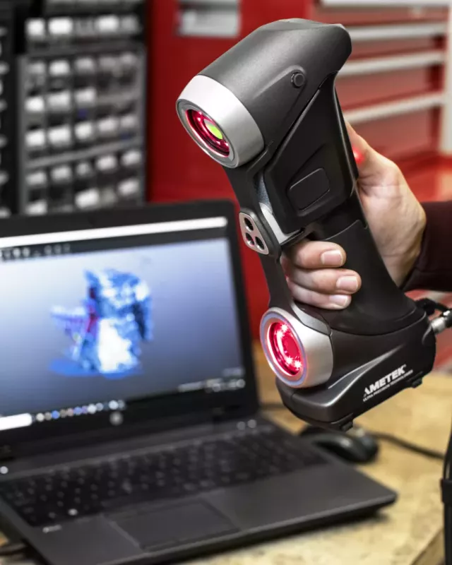 Operator skanuje element przemysłowy skanerem HandySCAN 3D Creaform obok laptopa z&nbsp;modelem 3D