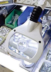 Głowica lampy z&nbsp;lupą Luxo WAVE LED nad drobnymi śrubami i&nbsp;elementami