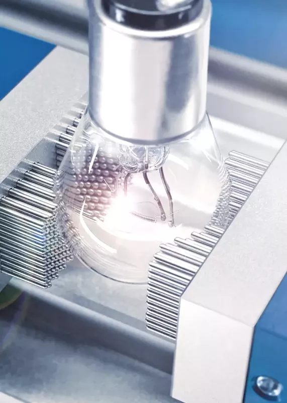 Żarówka uchwycona przez piny MATRIX; delikatny element stabilnie podparty bez ryzyka uszkodzeń podczas kontroli jakości lub montażu.