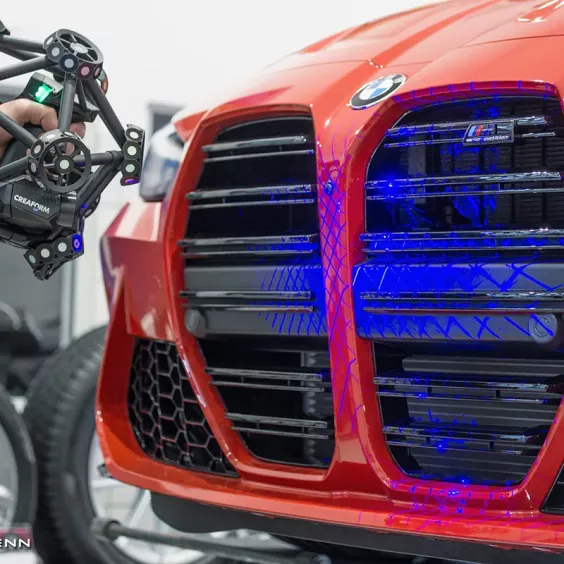 Skaner 3D Creaform MetraSCAN 3D skanuje grill czerwonego BMW M3 – niebieskie linie laserowe podczas precyzyjnego pomiaru karoserii