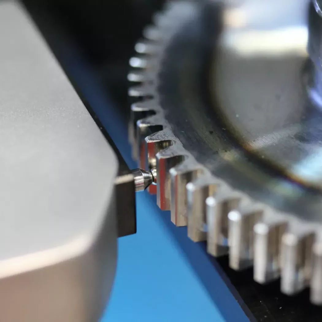 Zbliżenie na kulkę pomiarową dotykającą bok zęba koła na stanowisku pomiarowym.