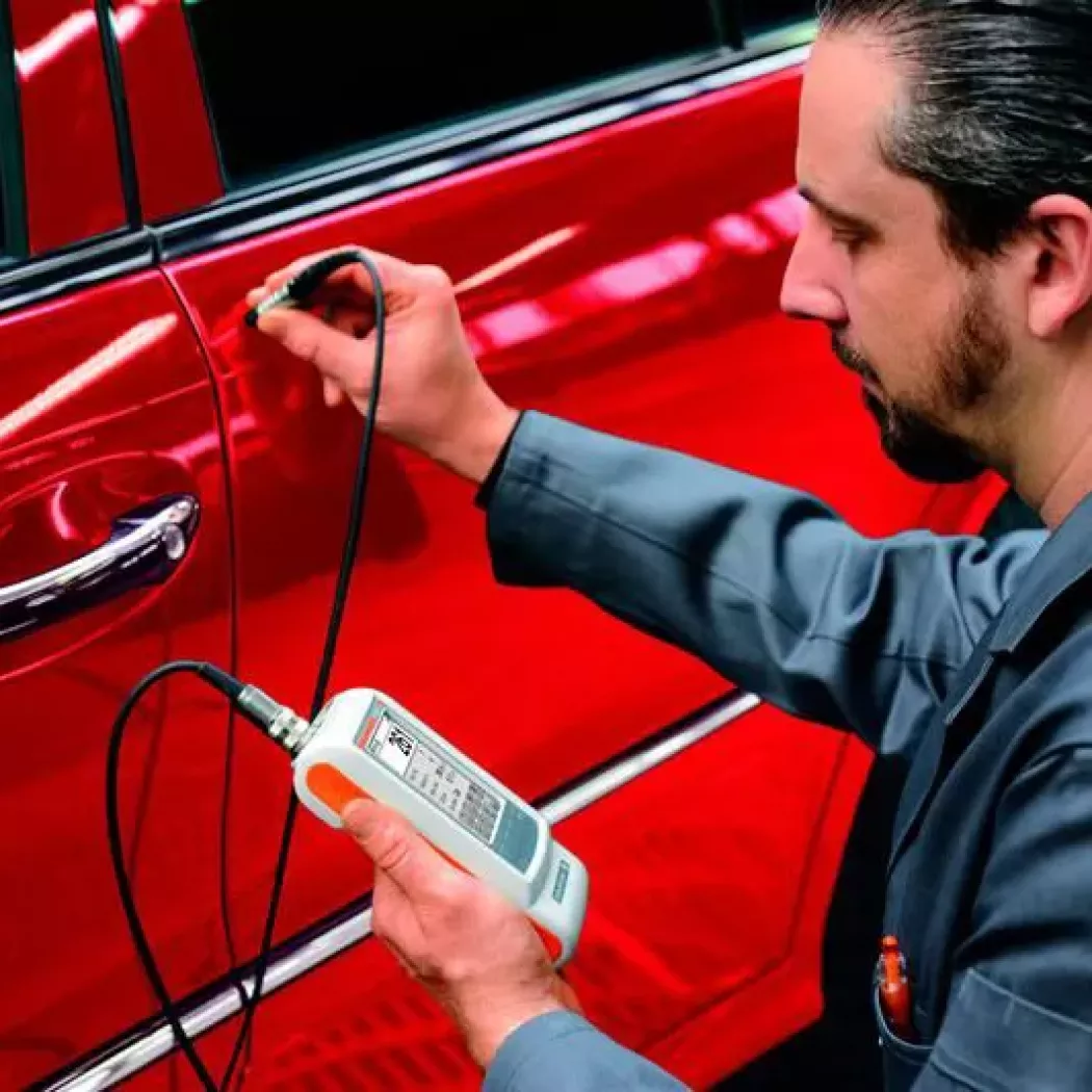 Technik wykonuje pomiar grubości powłoki lakierniczej na drzwiach samochodu miernikiem